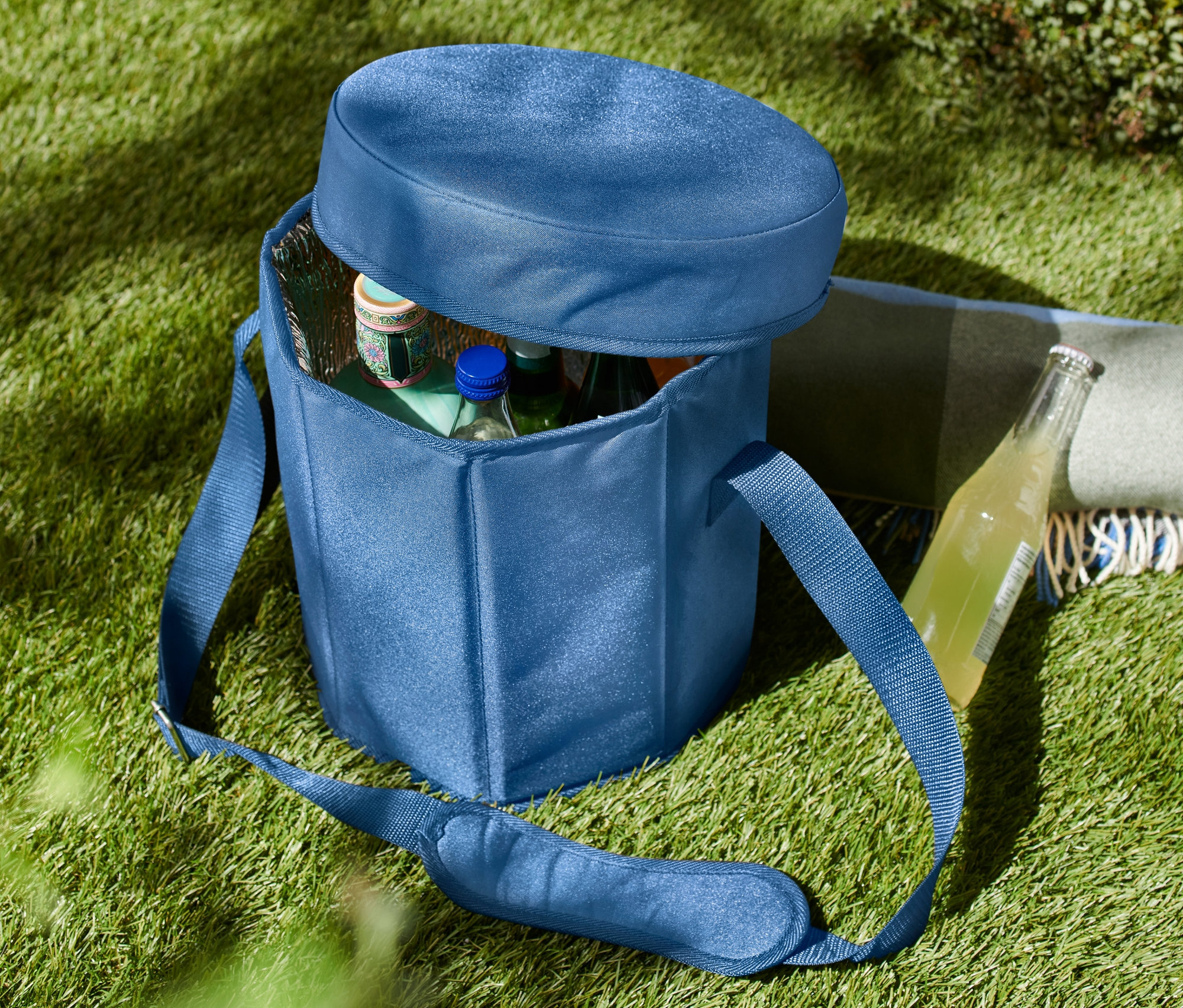 Niebieska torba termiczna 2 w 1 na trawie, częściowo otwarta, z butelkami w środku.