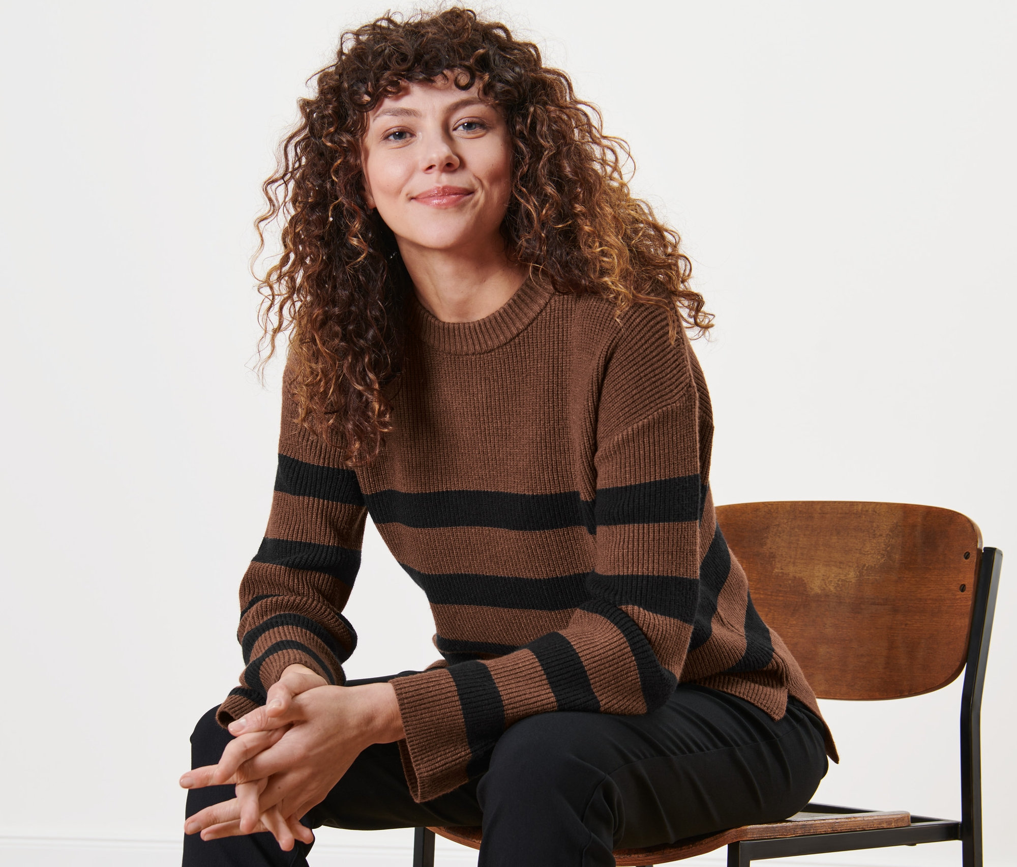 Kobieta siedzi na krześle i ma na sobie pasiasty sweter z dzianiny.