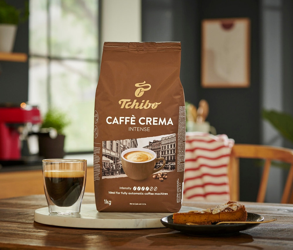 Opakowanie kawy ziarnistej Caffè Crema Intense 1 kg obok filiżanki kawy i kawałka ciasta.