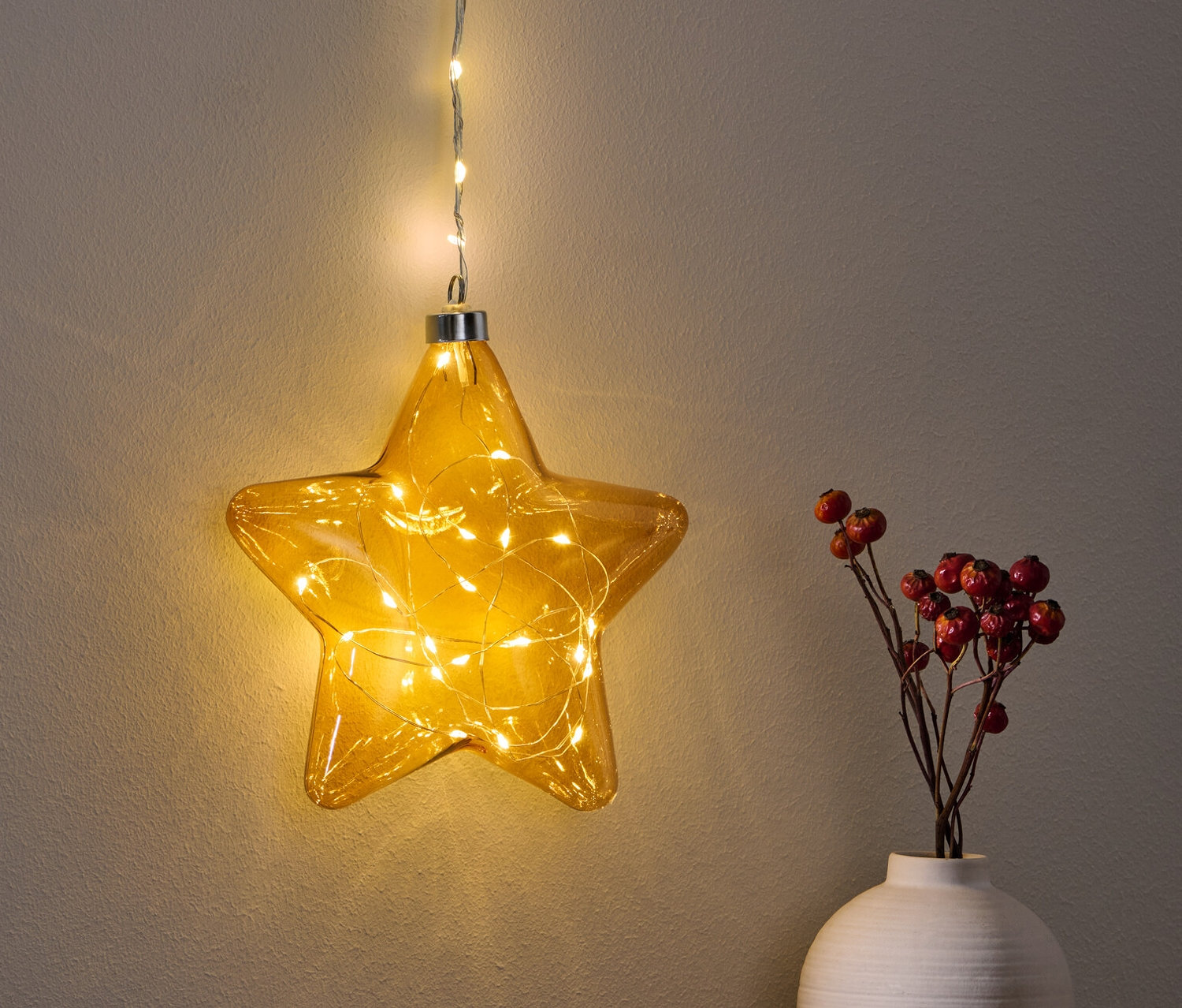 Wisząca gwiazda LED świeci nad stołem obok wazonu z czerwonymi jagodami.