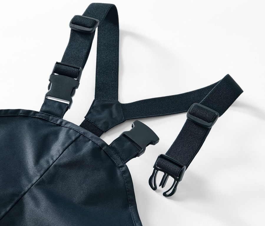 Detale spodni przeciwdeszczowych z czarnymi elastycznymi szelkami i plastikowymi klamrami na białym tle.