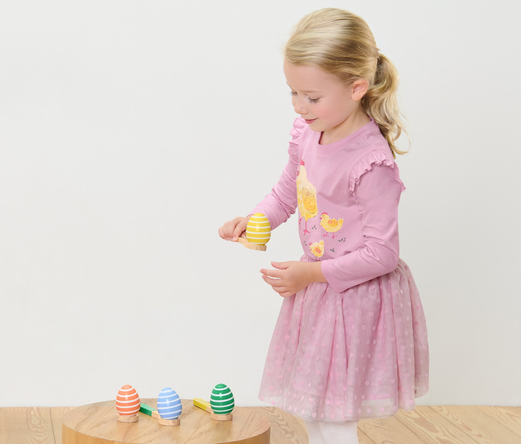 Dziewczynka gra w Grę „Wyścig z jajkami”. Stoi i koncentruje się na utrzymaniu równowagi jajka na łyżce.