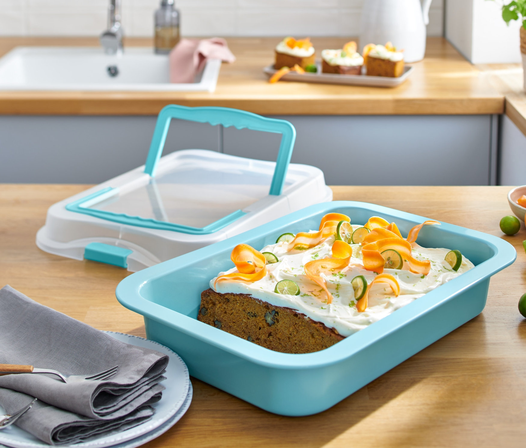 Blacha do pieczenia z pokrywką i upieczone ciasto z lukrem i dekoracjami z marchwi i limonki na drewnianym stole.