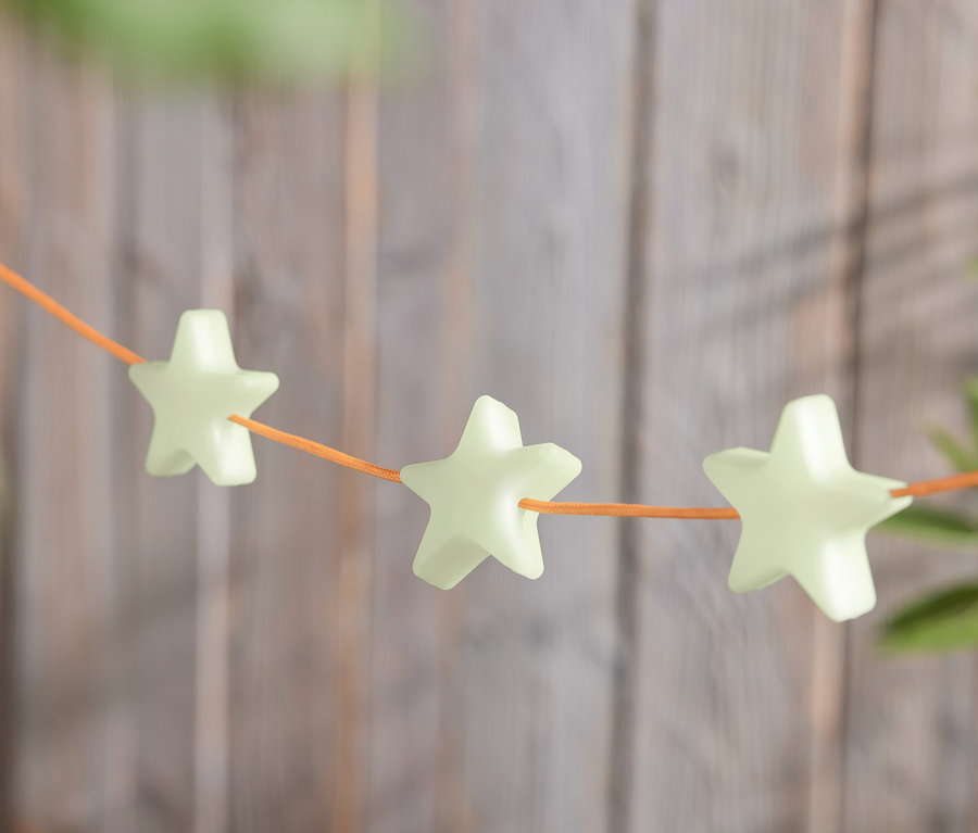 Rząd 8 świecących w nocy klipsów w kształcie gwiazdy, nawleczonych na pomarańczowy sznurek.