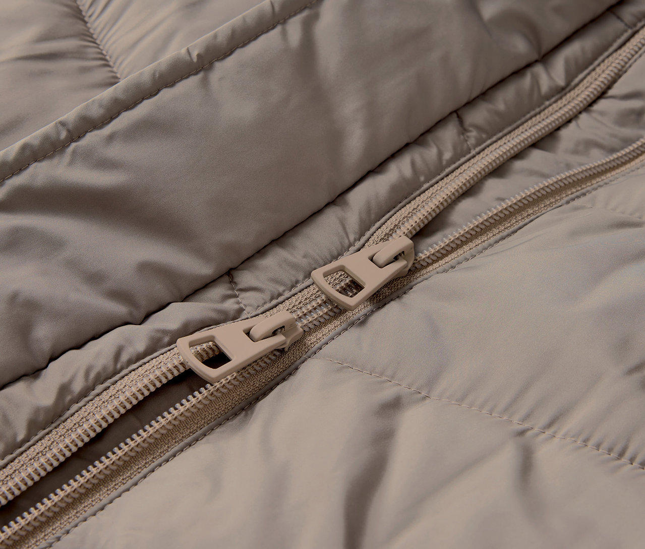 Zbliżenie na beżową kurtkę pikowaną z zamkiem błyskawicznym.