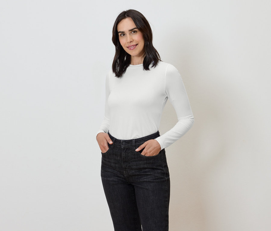 Kobieta z rękami w kieszeniach ciemnych dżinsów i białej koszulce z długim rękawem.