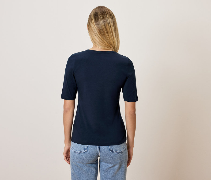 Z tyłu widać kobietę z blond włosami, ubraną w granatową koszulkę i niebieskie dżinsy.