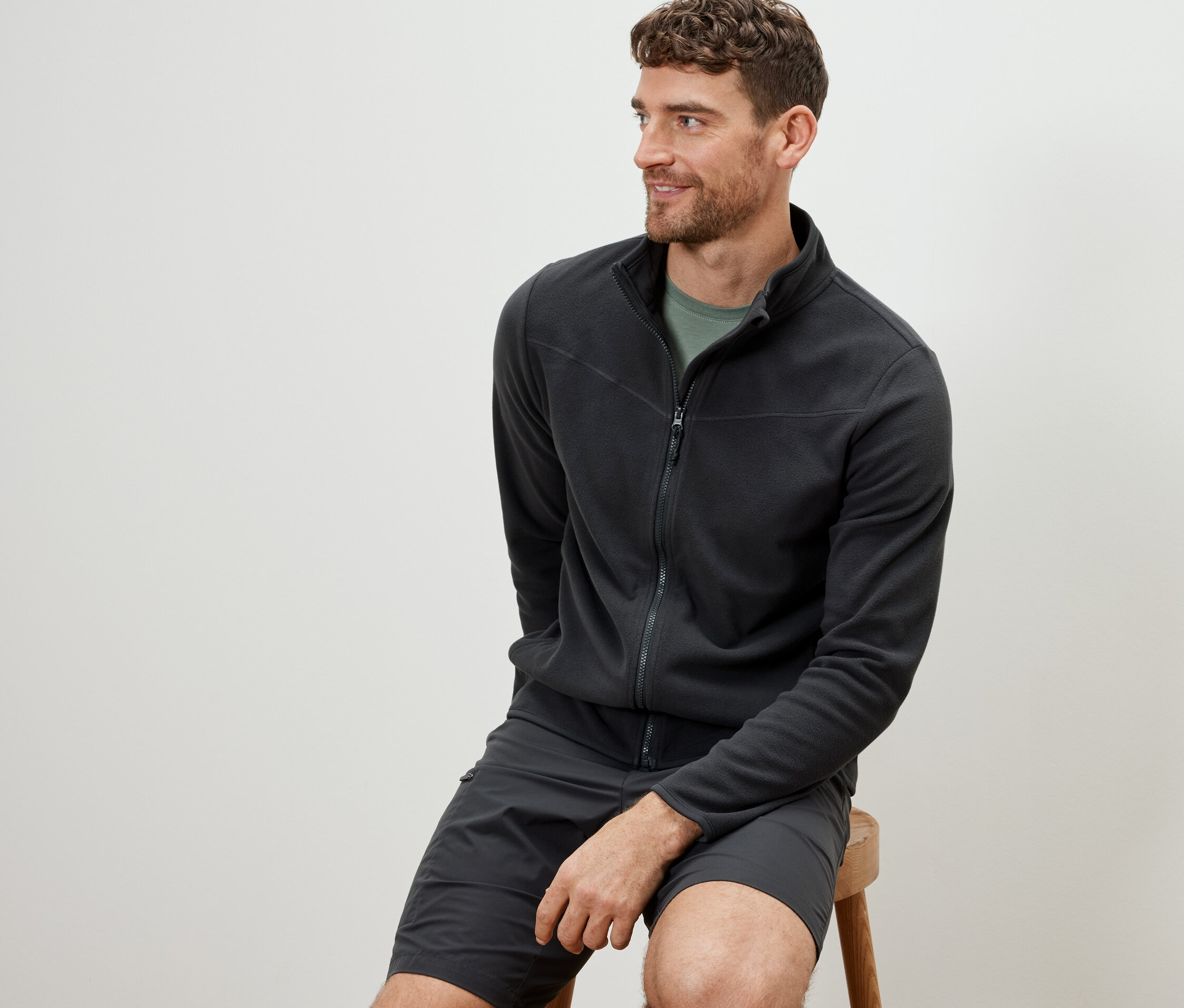 Mężczyzna siedzi na stołku i ma na sobie antracytową bluzę z polaru.