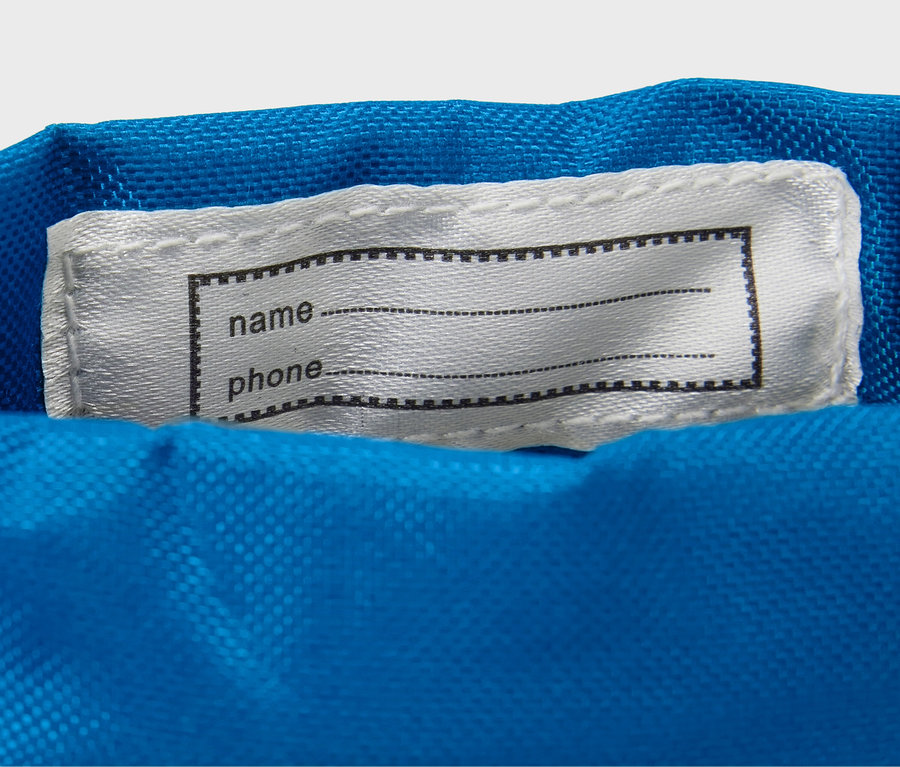 Na niebieskim materiale naszyta jest biała etykieta z czarną ramką na imię i nazwisko oraz numer telefonu.
