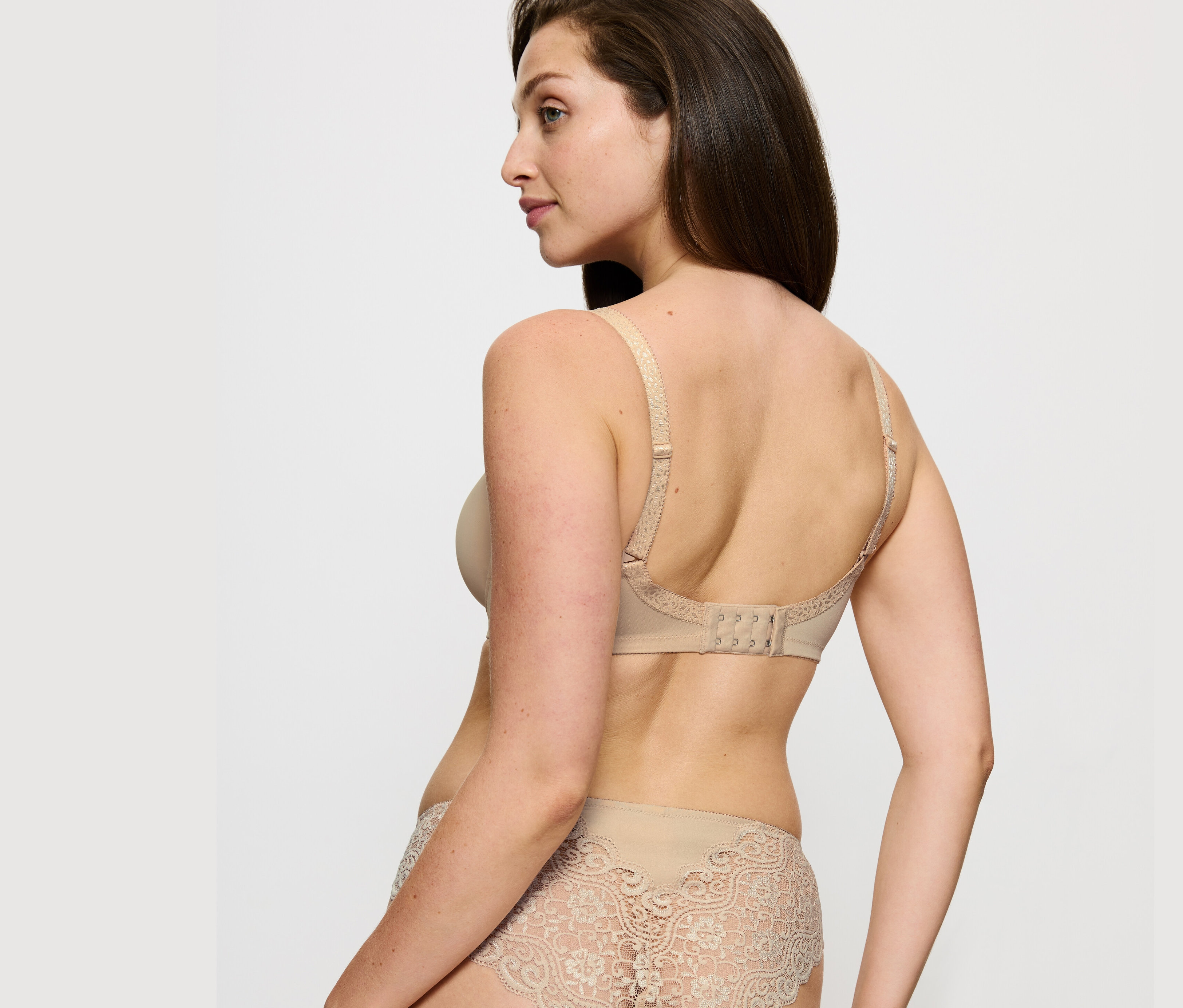 Kobieta pozuje w biustonoszu Triumph Amourette Minimizer w kolorze skóry i koronkowych majtkach.