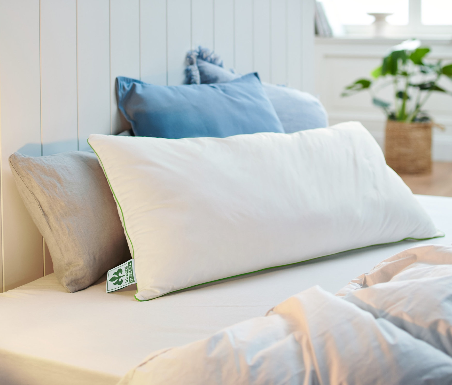 Na łóżku leży biała poduszka irisette® greenline o wymiarach ok. 80 x 40 cm.