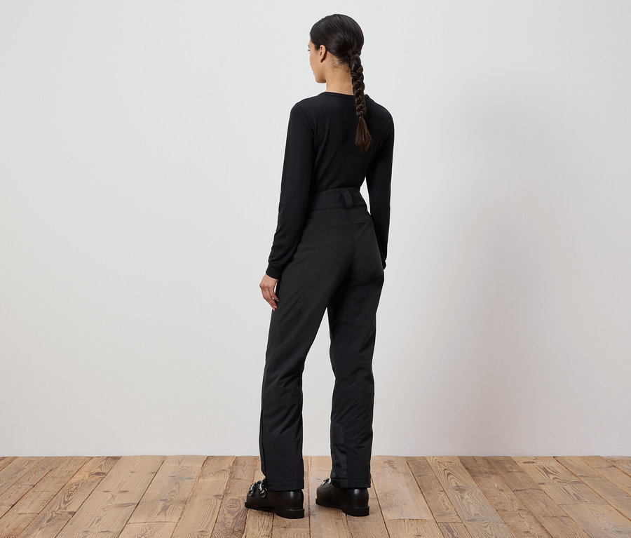 Kobieta w czarnym swetrze i spodniach stoi tyłem do kamery.