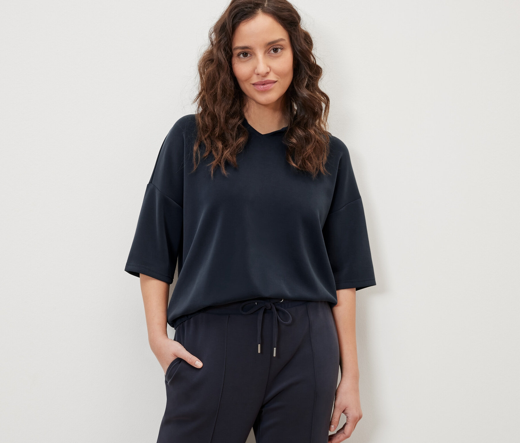 Kobieta pozuje w granatowej bluzie z kapturem z mieszanki modalu i spodniach.