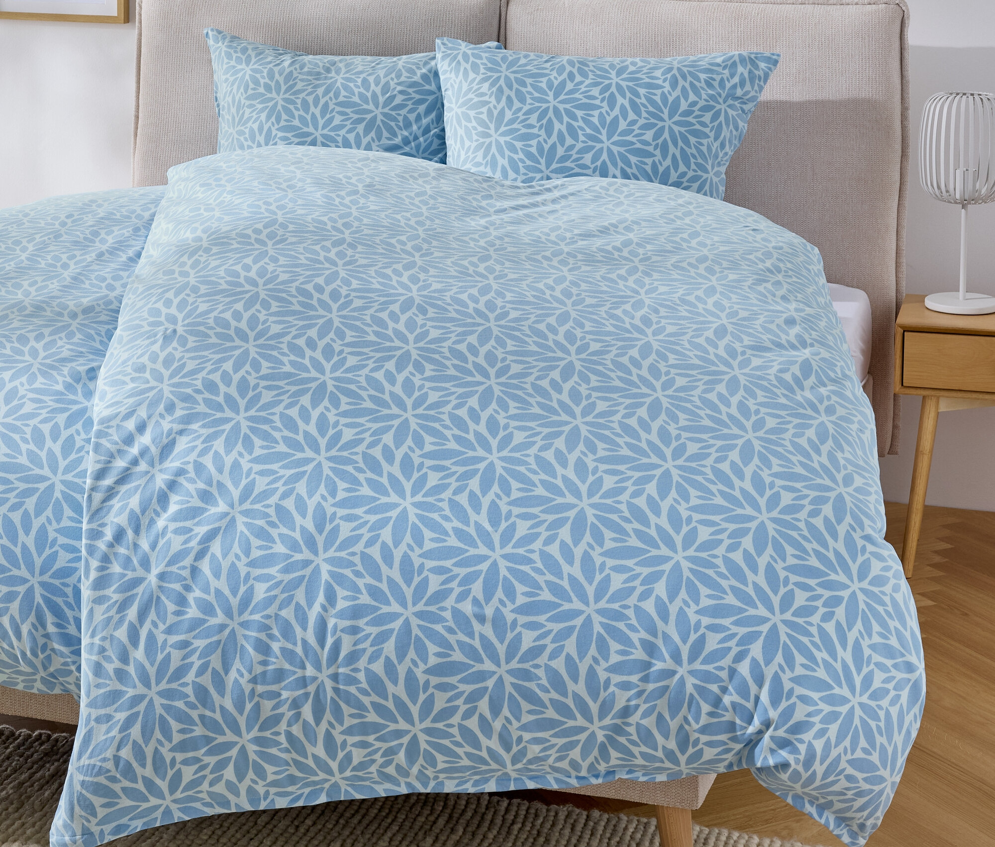 Łóżko z niebieską pościelą w kwiatowy wzór i dwiema poduszkami.