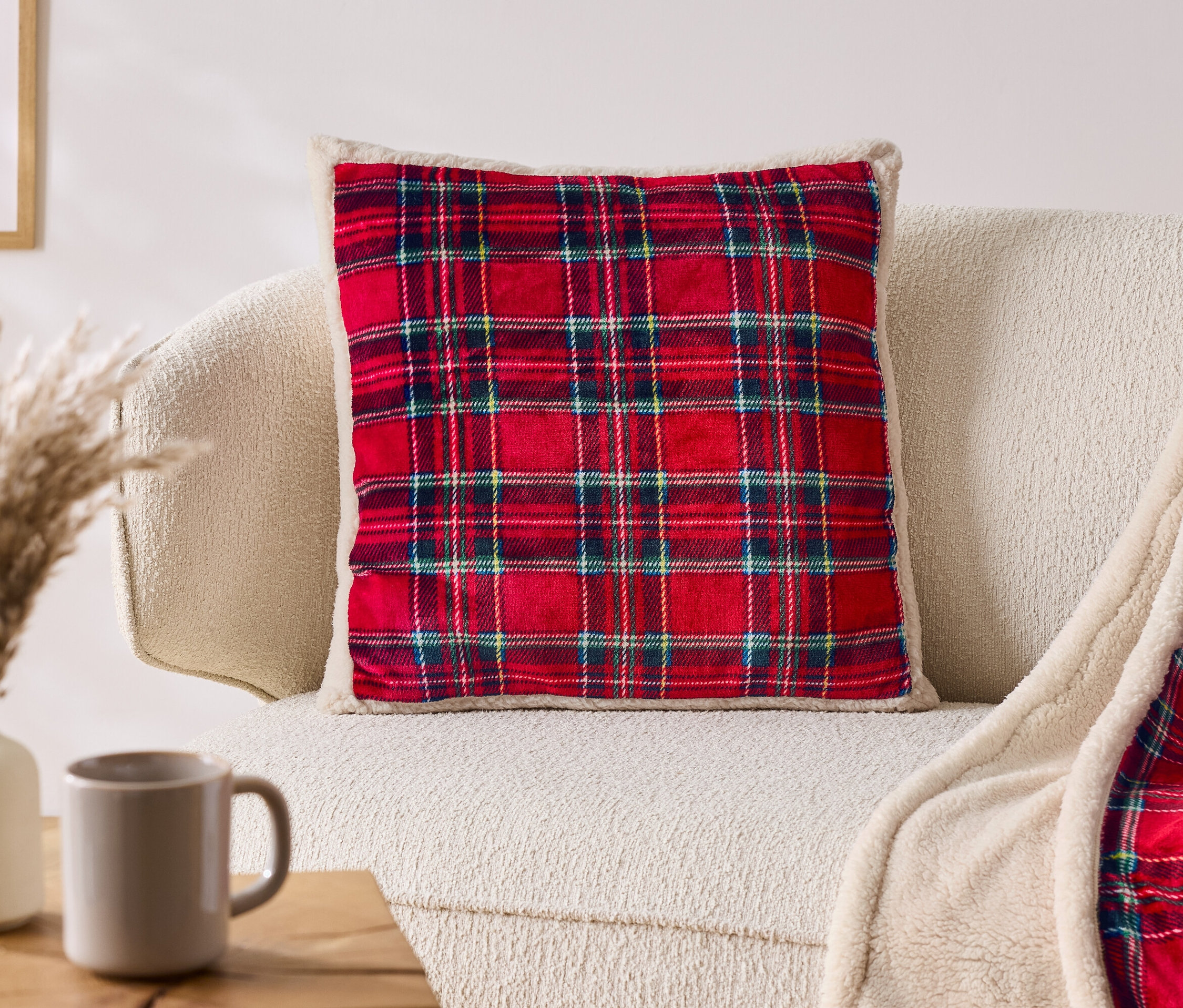 Czerwona poduszka w kratę leży na beżowej sofie obok koca w kratę.