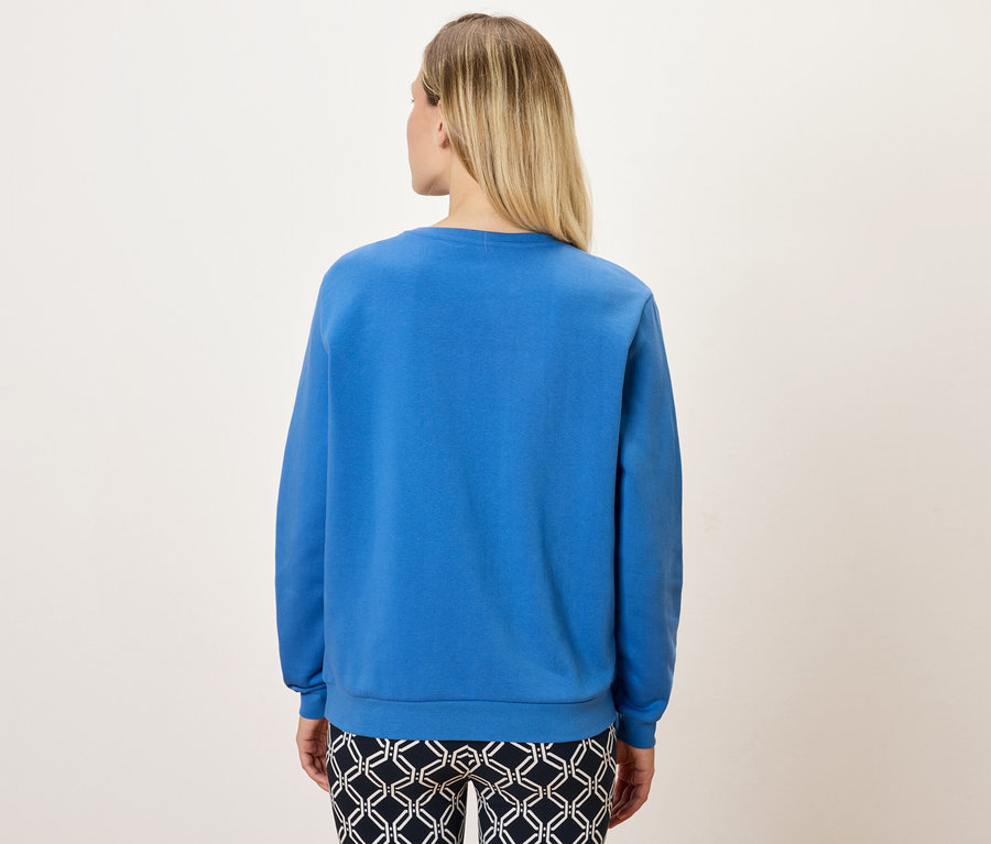 Widok z tyłu blondynki w niebieskiej bluzie i wzorzystych spodniach.