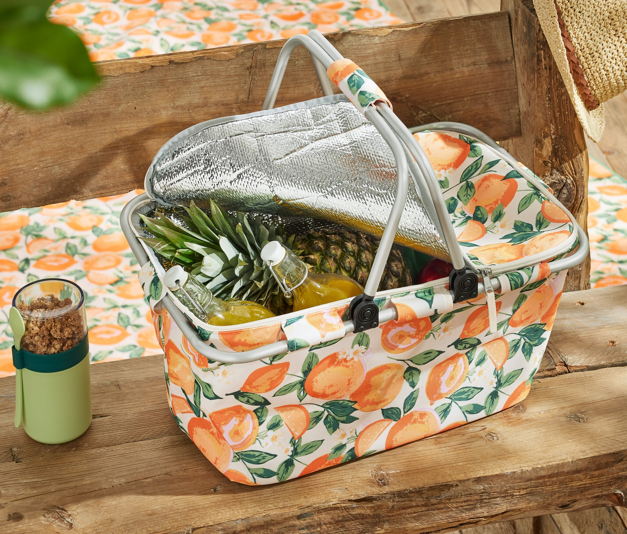 Koszyk termiczny z owocami i napojami na drewnianym stole.