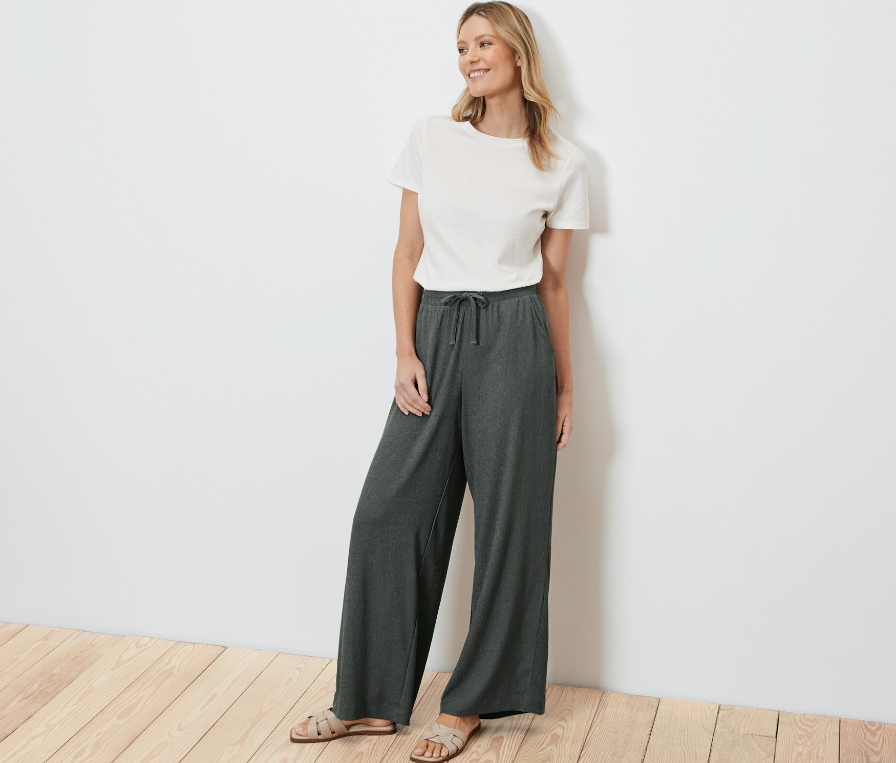 Kobieta stoi, ubrana w zielone spodnie na gumce z efektem marszczenia i biały t-shirt.