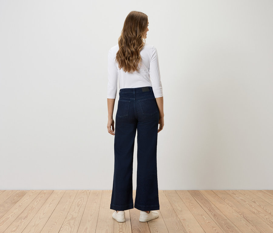 Kobieta stoi tyłem, ubrana w ciemnoniebieskie, szerokie dżinsy i biały top.