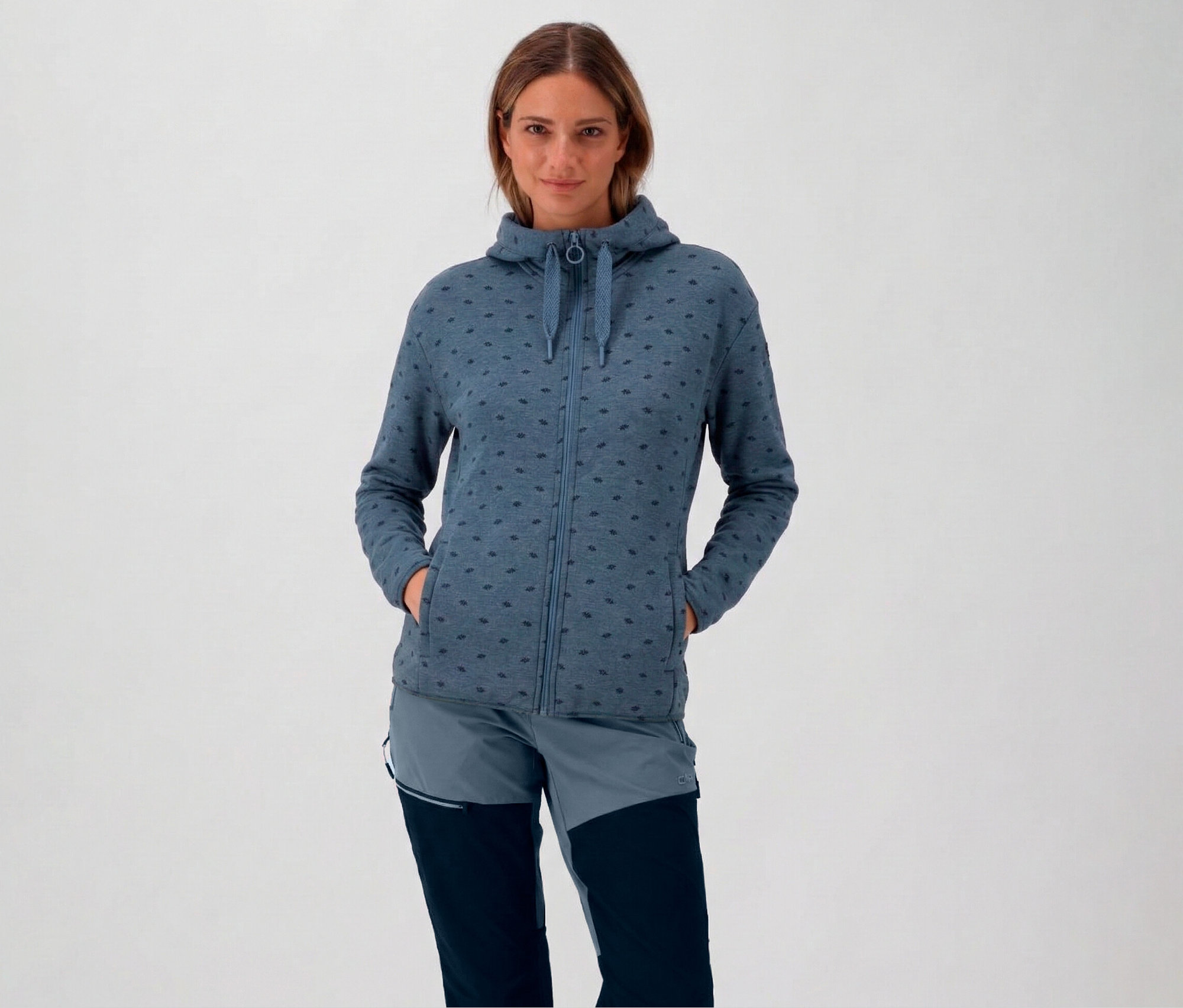 Kobieta w kapturze i niebieskiej bluzie polarowej CMP z kapturem, z rękami w kieszeniach.