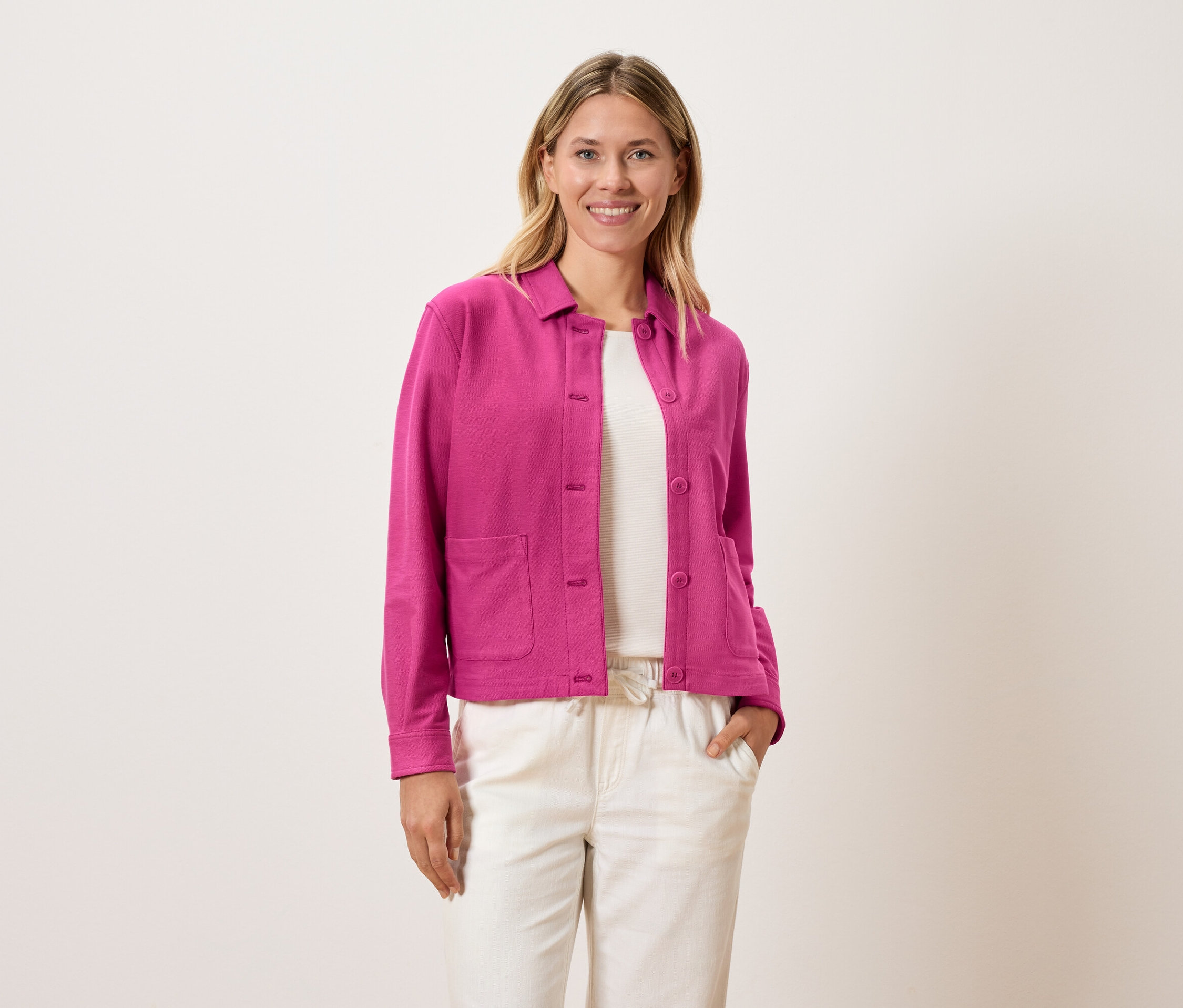 Kobieta ma na sobie różową kurtkę nałożoną na biały top i kremowe spodnie.