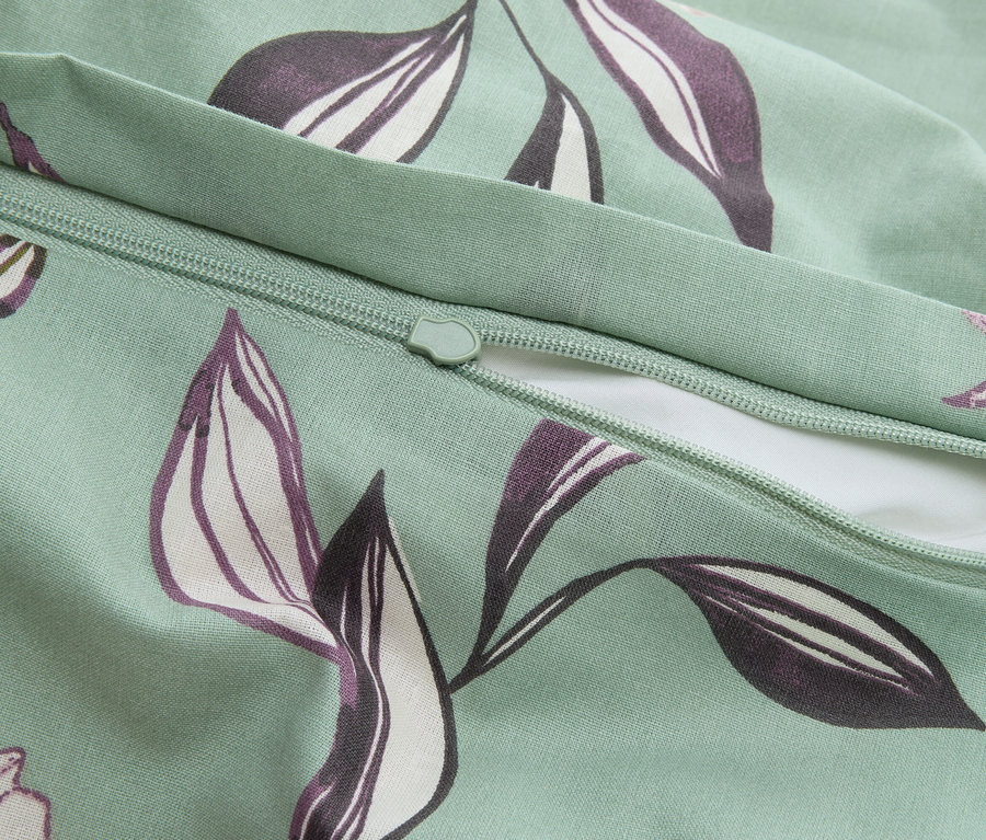 Zbliżenie miętowej poszewki na poduszkę z zamkiem błyskawicznym i fioletowym wzorem liści.