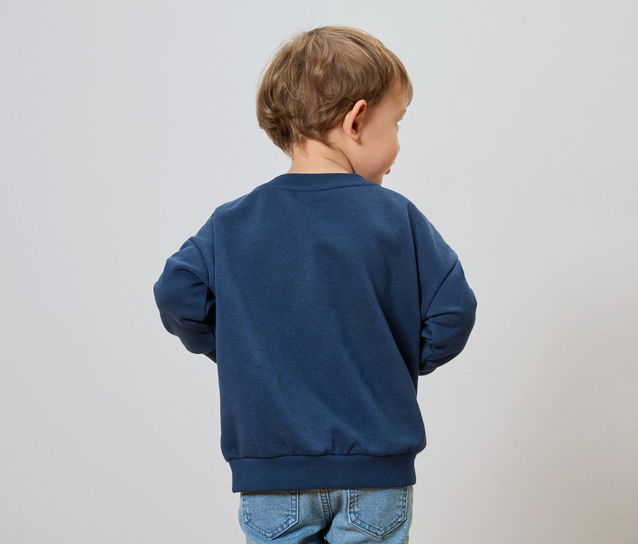 Chłopiec o blond włosach ma na sobie granatową bluzę i dżinsy.