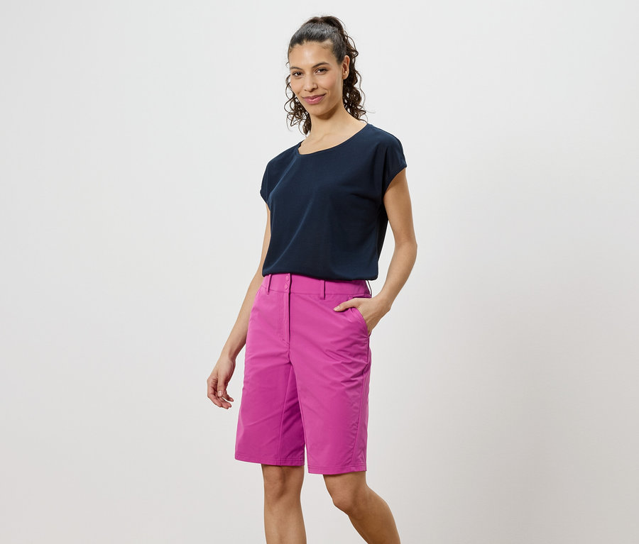 Kobieta w ciemnym T-shircie i różowych szortach stoi na białym tle.