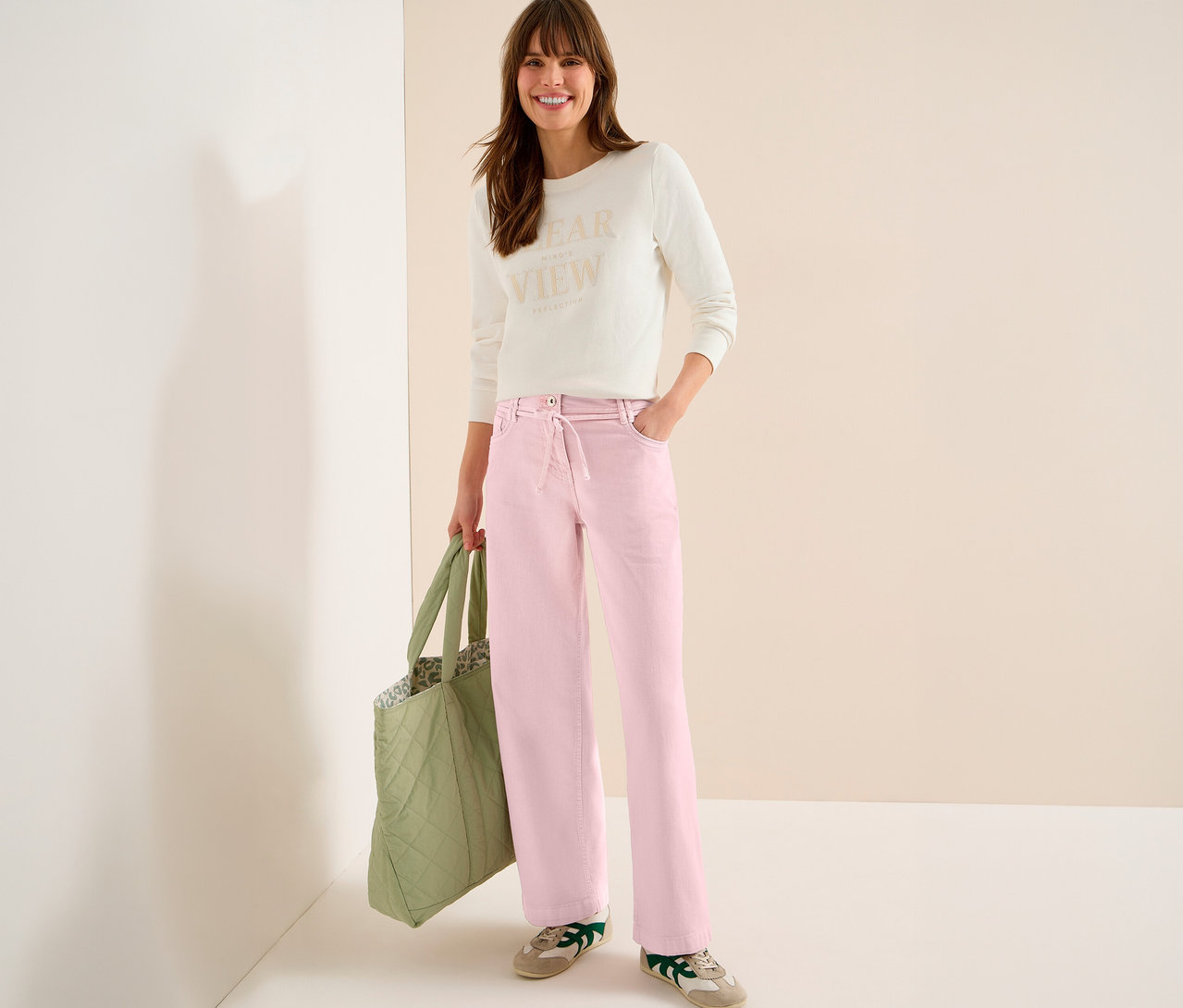 Kobieta z torbą nosi jasny top i dżinsy CECIL „Neele” w kolorze różowym.