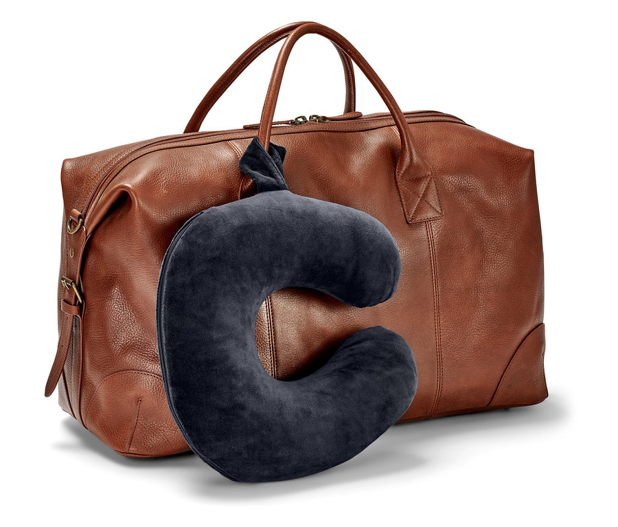 Ciemnoniebieska poduszka na szyję wisi przed brązową torbą podróżną.