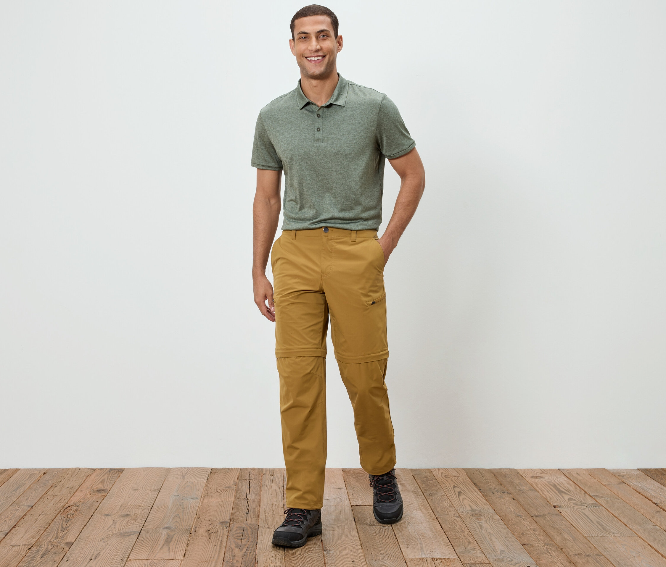 Mężczyzna stoi na tle białej ściany, ubrany w zieloną koszulkę polo i spodnie khaki.