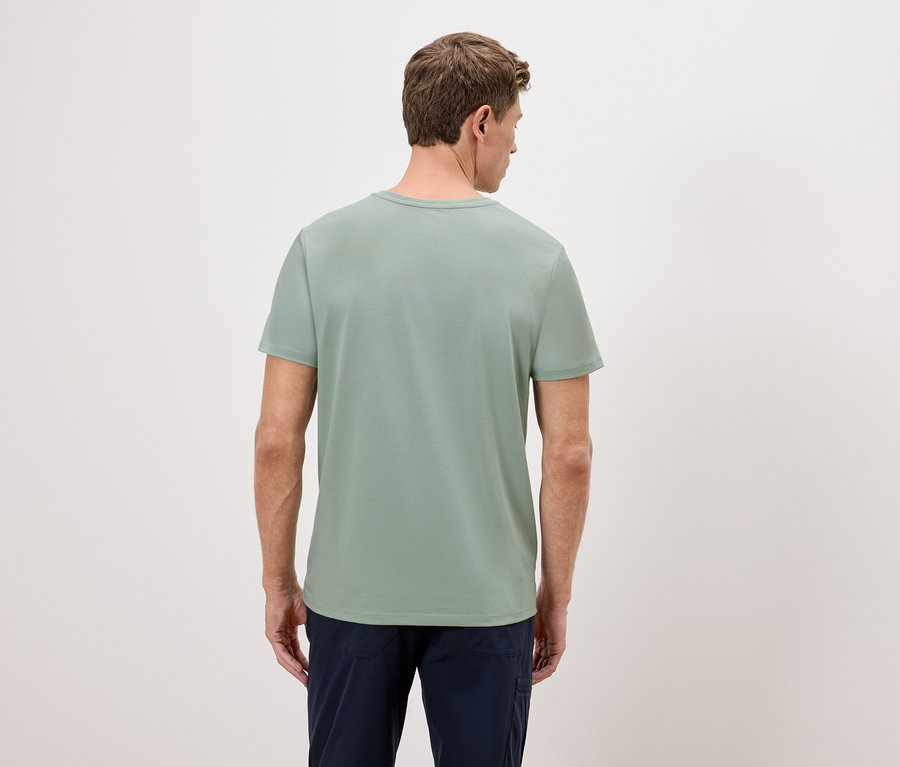 Mężczyzna stoi tyłem do kamery, ubrany w zielony T-shirt i niebieskie spodnie.