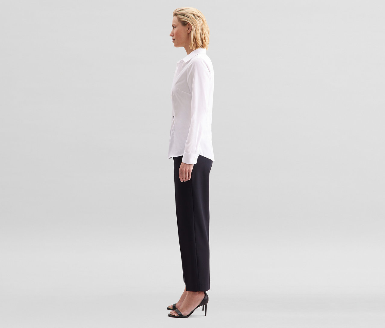Kobieta z profilu, ubrana w białą bluzkę Seidensticker Slim Fit non iron i czarne spodnie.