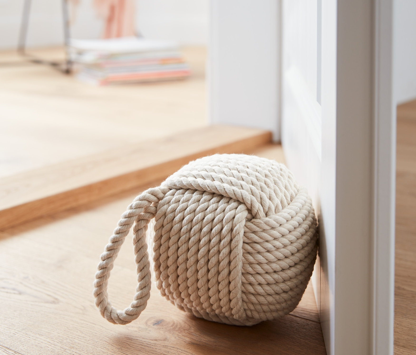 Stoper do drzwi ze sznura leży przy białych drzwiach na drewnianej podłodze.