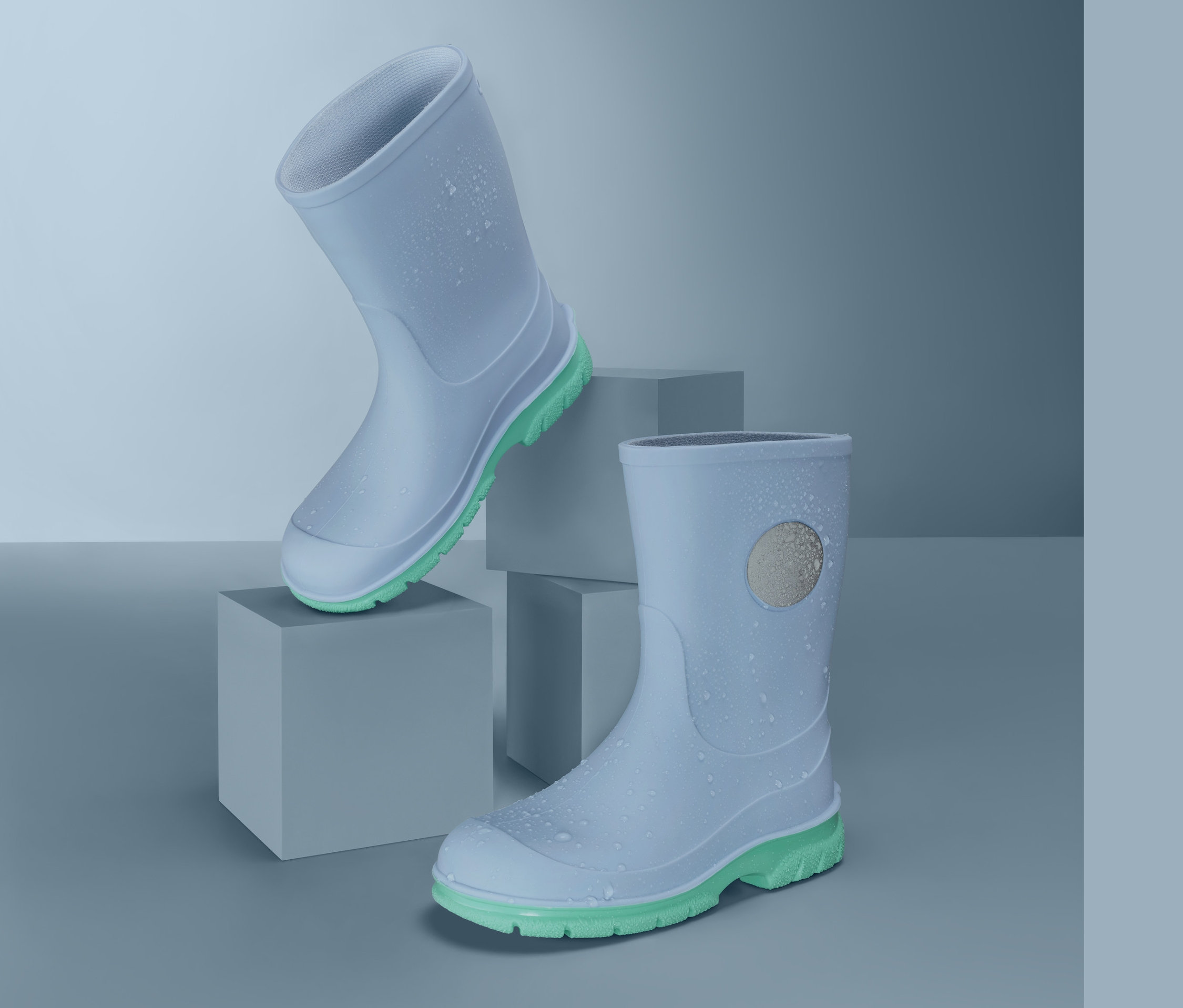 Dwa jasnoniebieskie kalosze z limonkowo-zielonymi podeszwami na szarych kostkach.