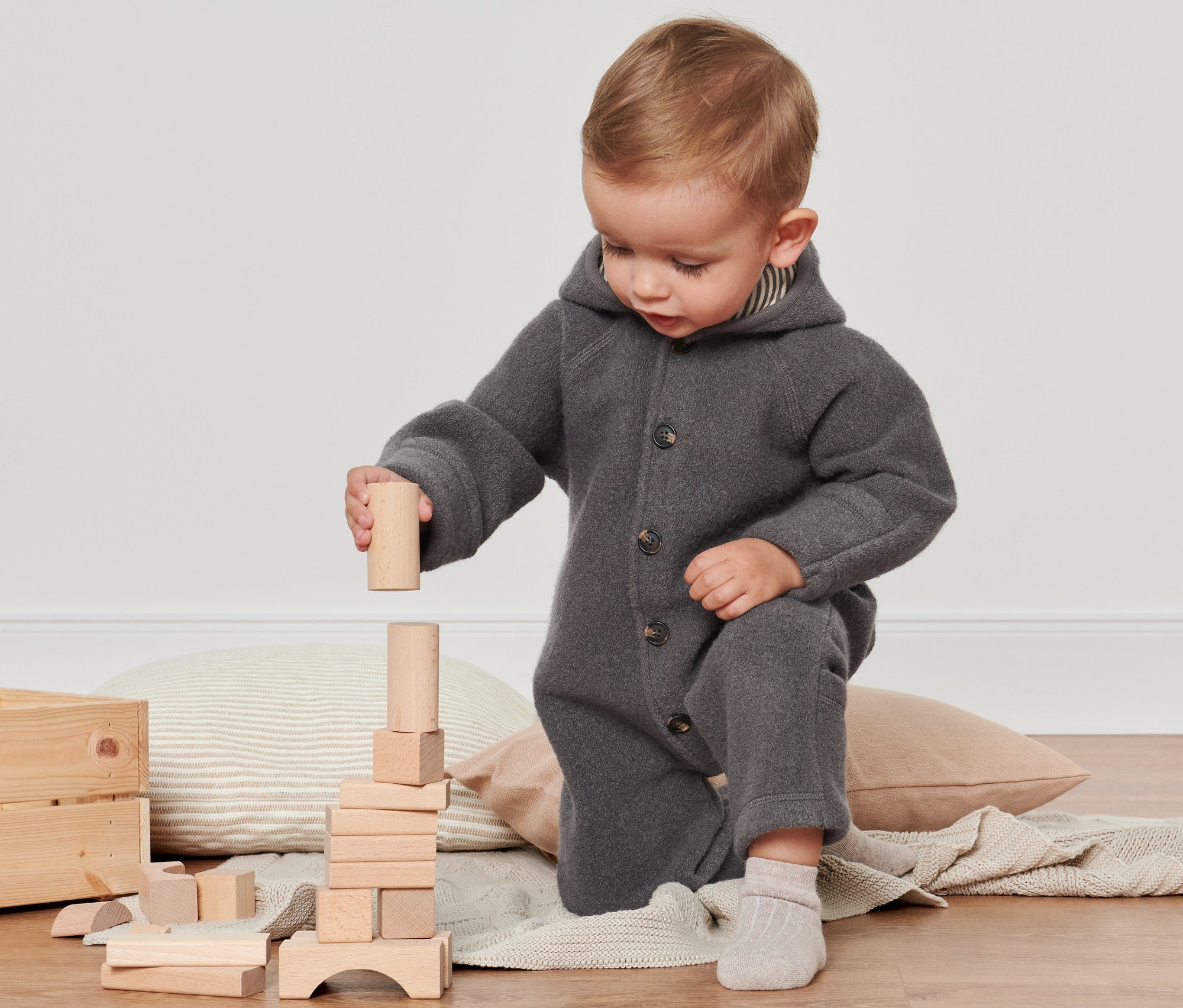 Dziecko bawi się drewnianymi klockami, ubrane w szary kombinezon z wełną z certyfikatem RWS.
