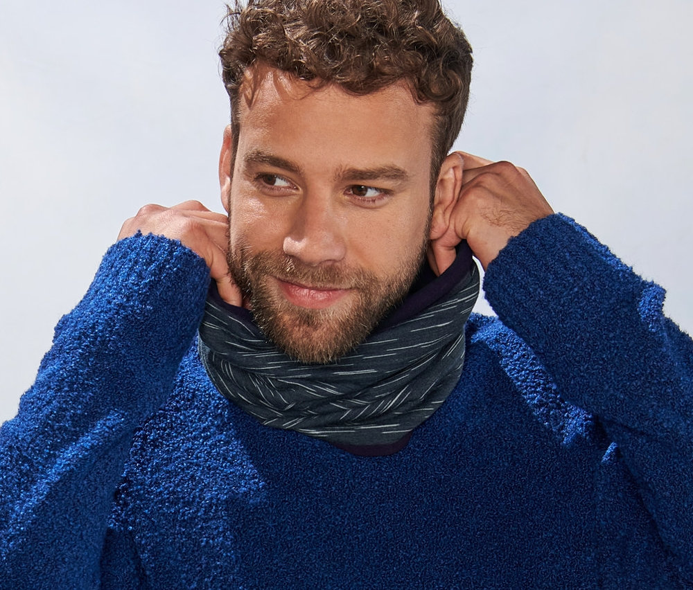 Mężczyzna poprawia antracytowy ciepłochronny kołnierz z polaru na szyi. W tle widoczne góry.