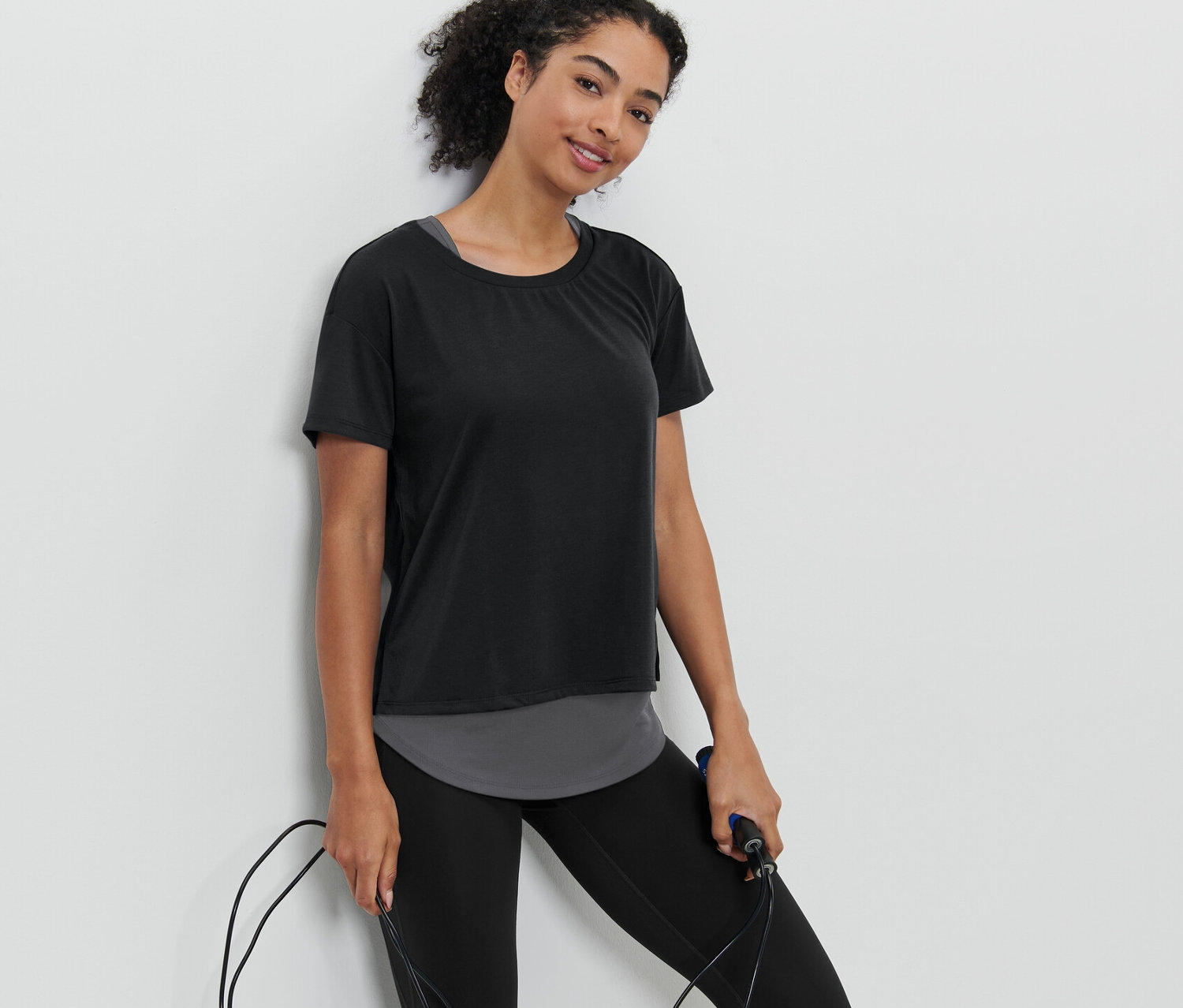 Kobieta trzyma skakankę i ma na sobie czarną koszulkę sportową z krótkim rękawem 2 w 1.