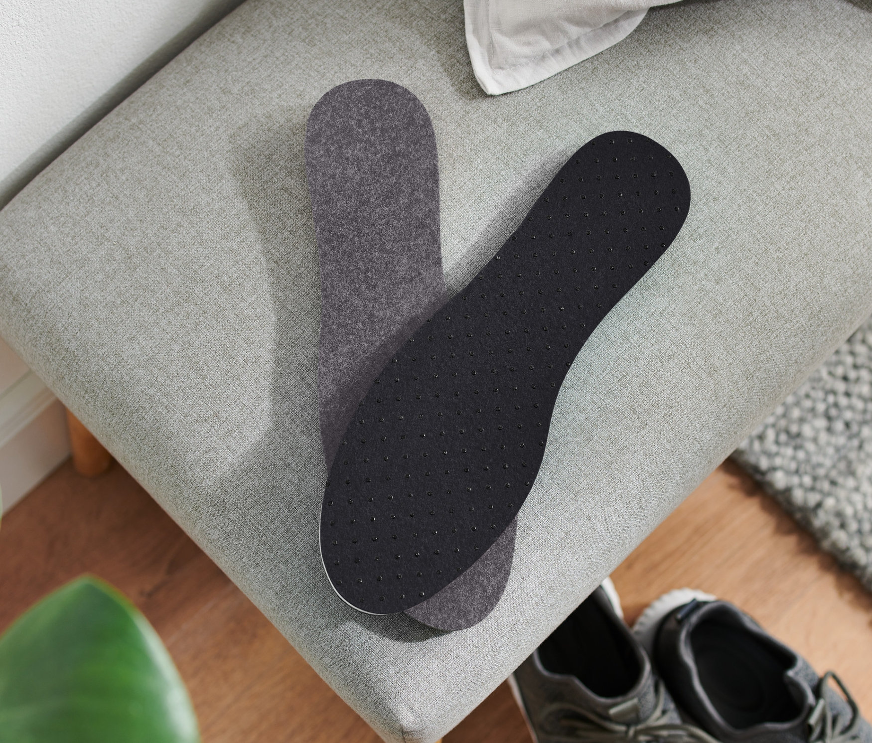 Dwie wkładki termiczne do butów leżą na szarej ławce obok pary szarych butów.