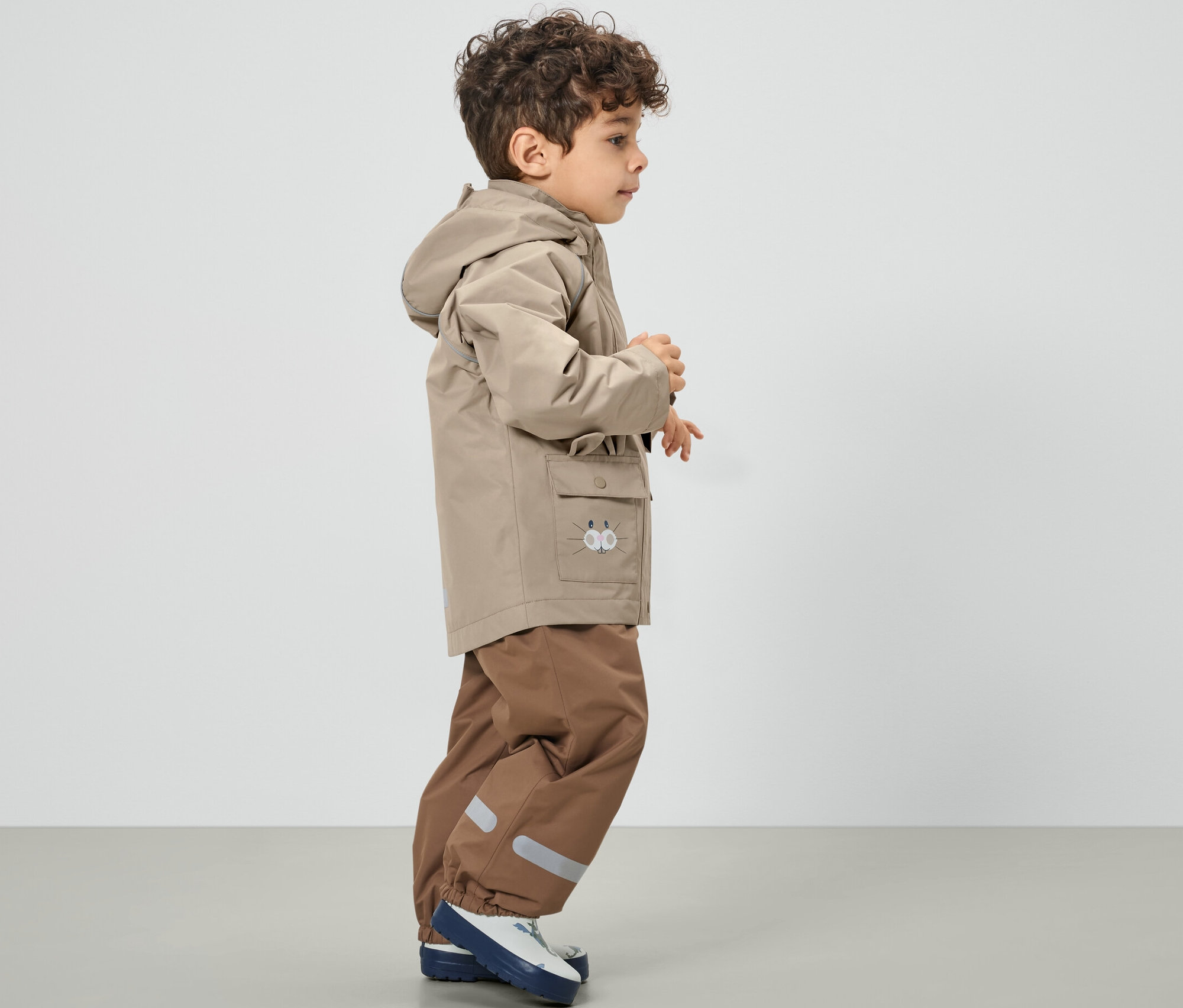 Chłopiec w beżowej kurtce przeciwdeszczowej.