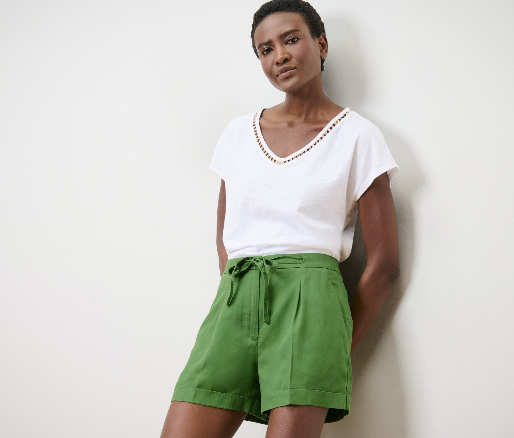 Kobieta pozuje w zielonych szortach lnianych i białym t-shircie.