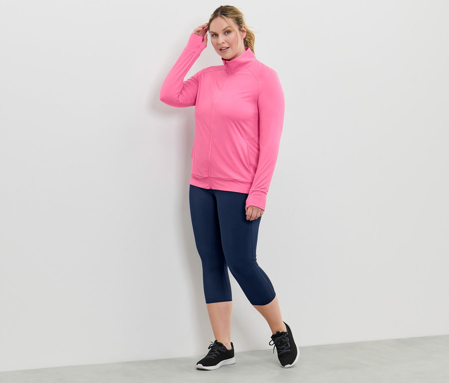 Kobieta ma na sobie różową funkcyjną bluzę rozpinaną i granatowe legginsy.