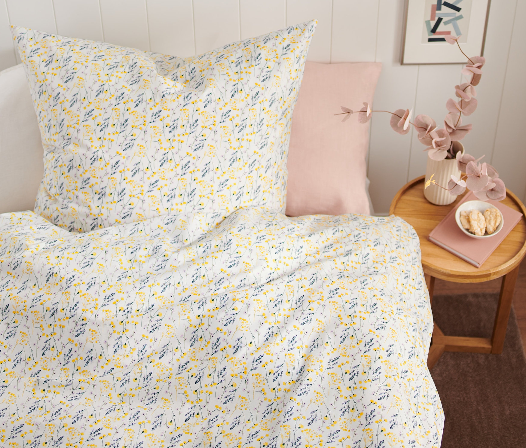 Kwiatowy wzór na pościeli bawełnianej premium o standardowej wielkości na łóżku. Obok łóżka stoi stół z wazonem i książką.