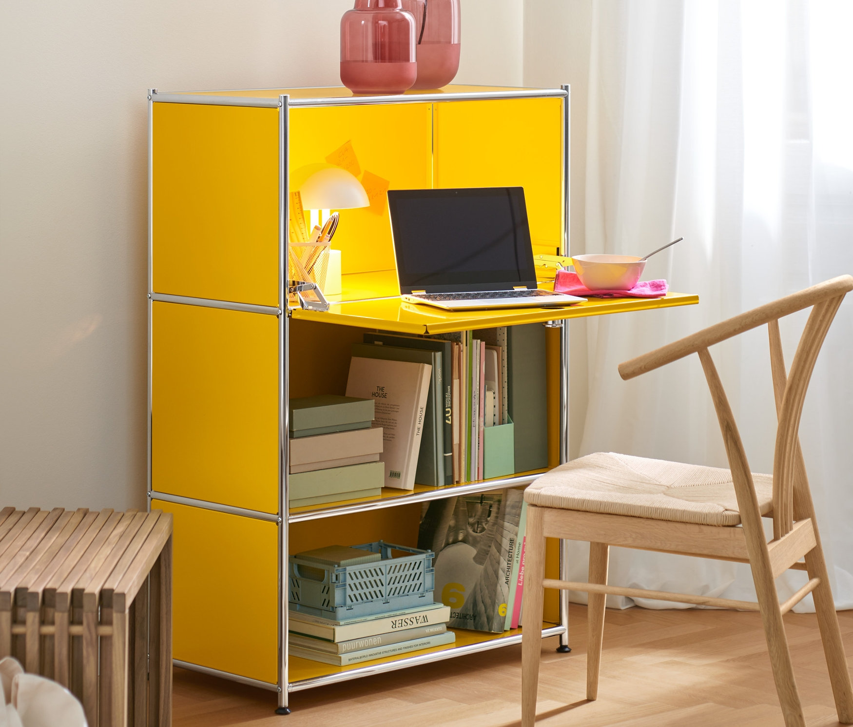 Żółty sekretarzyk „CN3” służy jako biurko z białą akumulatorową lampką stołową LED. Na górze stoją wazony. Obok stoi rozsuwana ławka.