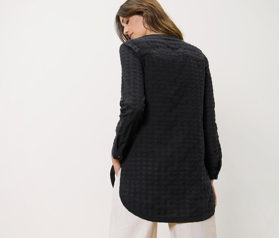 Kobieta ma na sobie długą tunikę o strukturze tkaniny i spodnie.