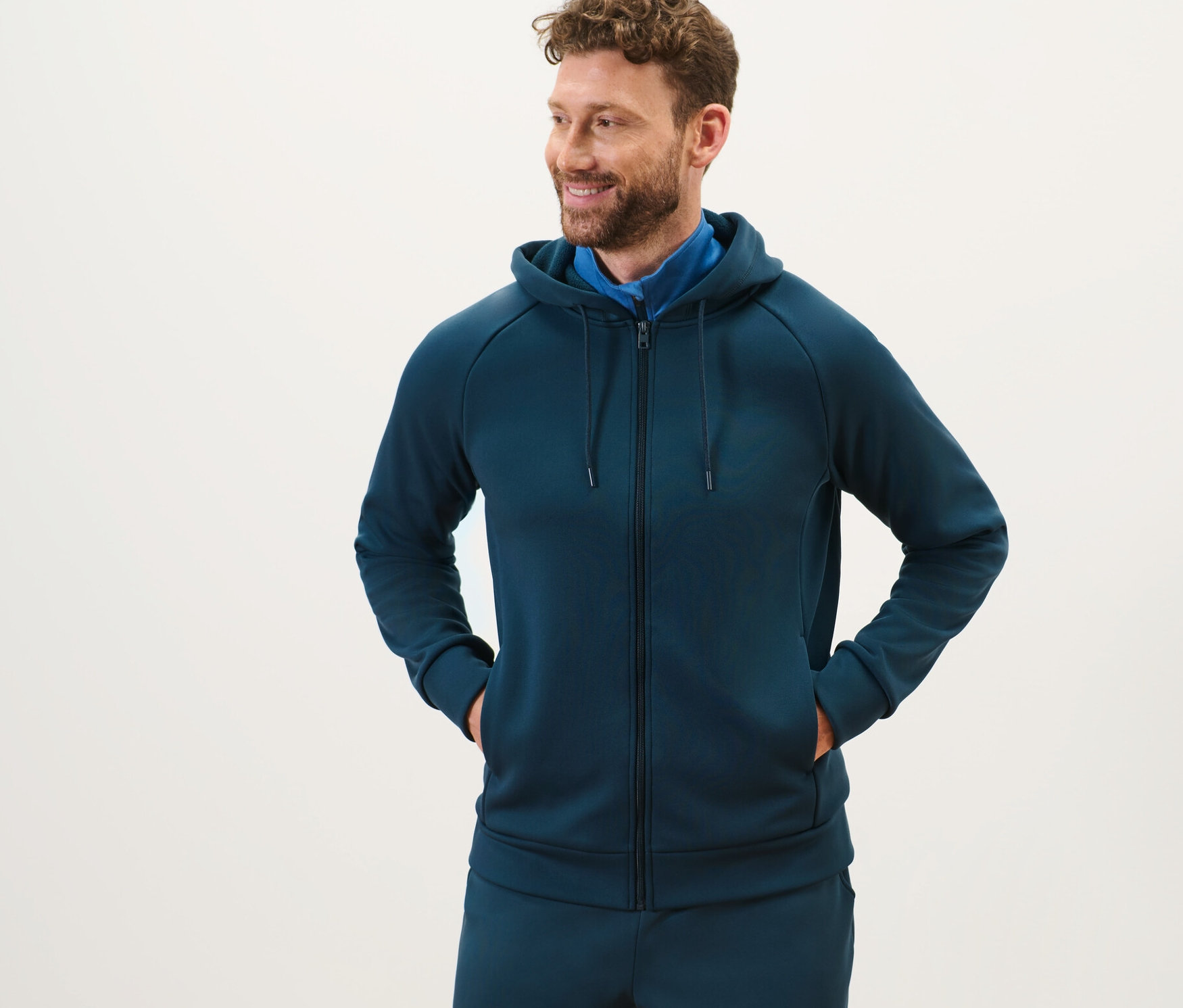 Mężczyzna z brodą stoi i ma na sobie bluzę funkcyjną z kapturem.