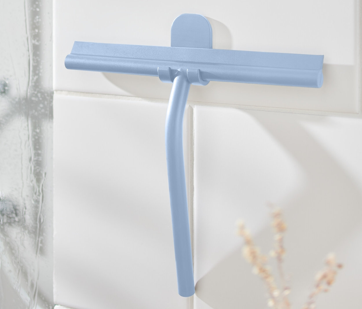 Niebieska ściągaczka do wody z uchwytem ściennym na białych kafelkach obok prysznica.