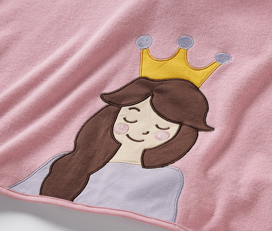 Zbliżenie na różowe ponczo z tkaniny frotte z aplikacją przedstawiającą księżniczkę z brązowymi włosami i złotą koroną.