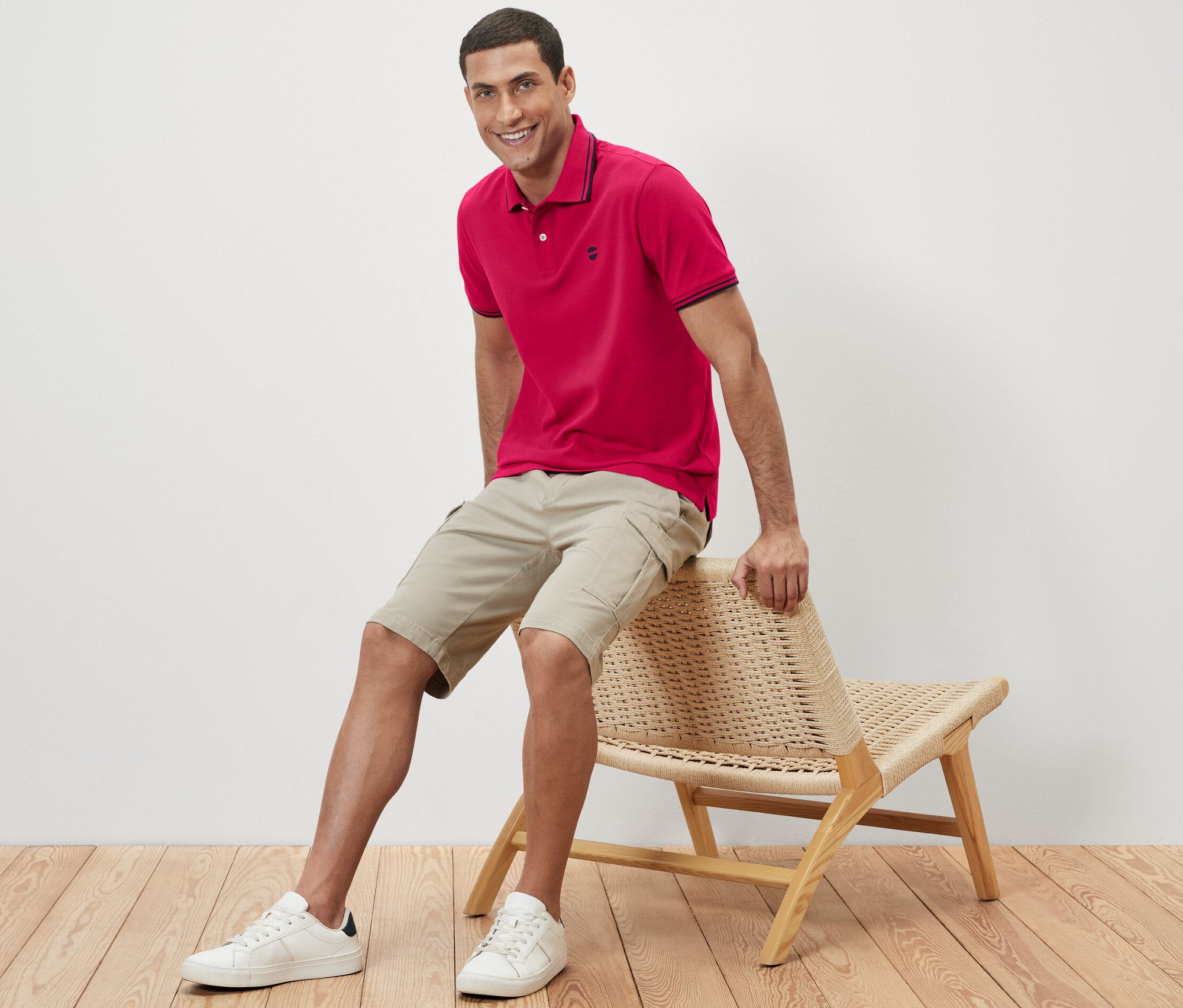 Mężczyzna siedzi na wiklinowym krześle i ma na sobie różową koszulkę polo.