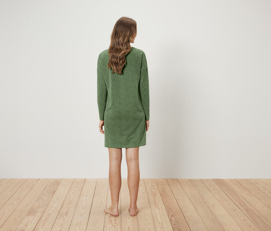 Kobieta stoi tyłem do kamery i ma na sobie zieloną sukienkę.